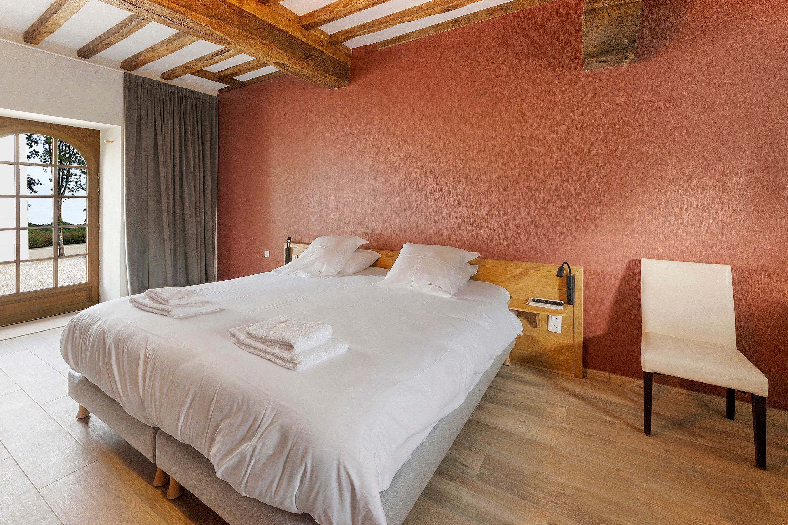 Une chambre d’hôtel avec un grand lit, une tête de lit en bois, une table de chevet avec une lampe et une chaise.
