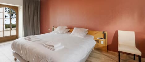 Une chambre d’hôtel avec un grand lit, une tête de lit en bois, une table de chevet avec une lampe et une chaise.