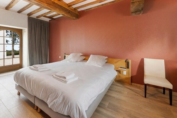 Une chambre d’hôtel avec un grand lit, une tête de lit en bois, une table de chevet avec une lampe et une chaise.