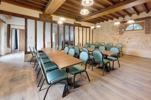 Ein Konferenzraum mit einem langen Holztisch, mehreren Stühlen, einer Steinwand und Holzbalken an der Decke.