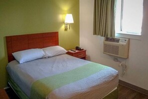 Una habitación de hotel con cama, lámpara de noche, teléfono y aire acondicionado.