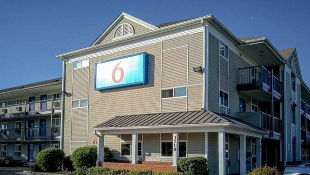 Um motel com um grande letreiro em forma de '6', varanda coberta e alicerce de tijolos.