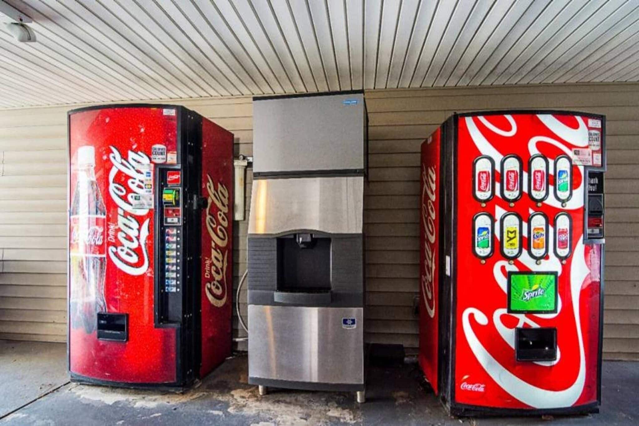 Three beverage vending machines, one with a silver top and two with red and white branding, against a plain wall.