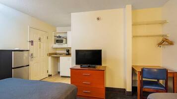 A hotel room with a bed, a desk with a chair, a television, a microwave, and a refrigerator.