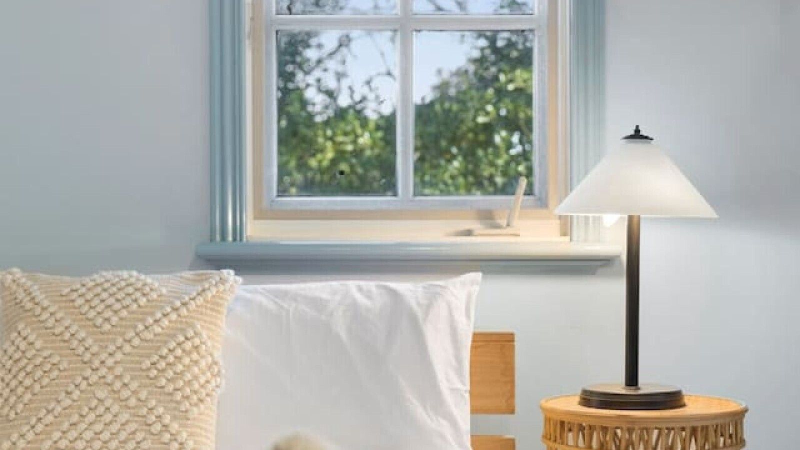 Ett sovrum med en säng, ett sängbord med en lampa och ett fönster med utsikt över träd.