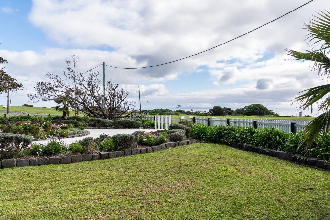 A landscaped garden with a curved pathway, a variety of plants, and a white fence.