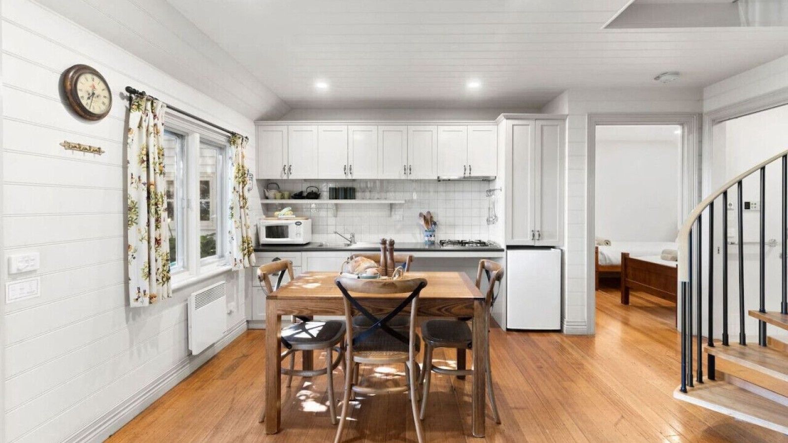 A modern kitchen with white cabinetry, a dining table with chairs, and a small refrigerator.