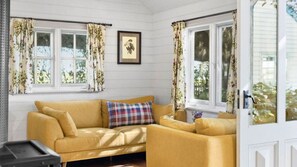 A room with a yellow sofa, floral curtains, and a framed botanical print on the wall.