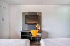 A hotel room with a bed, a desk with a chair, a flat-screen TV, and a lamp. - Spacious 2 Full Beds | Mini Fridge (Austin TX)