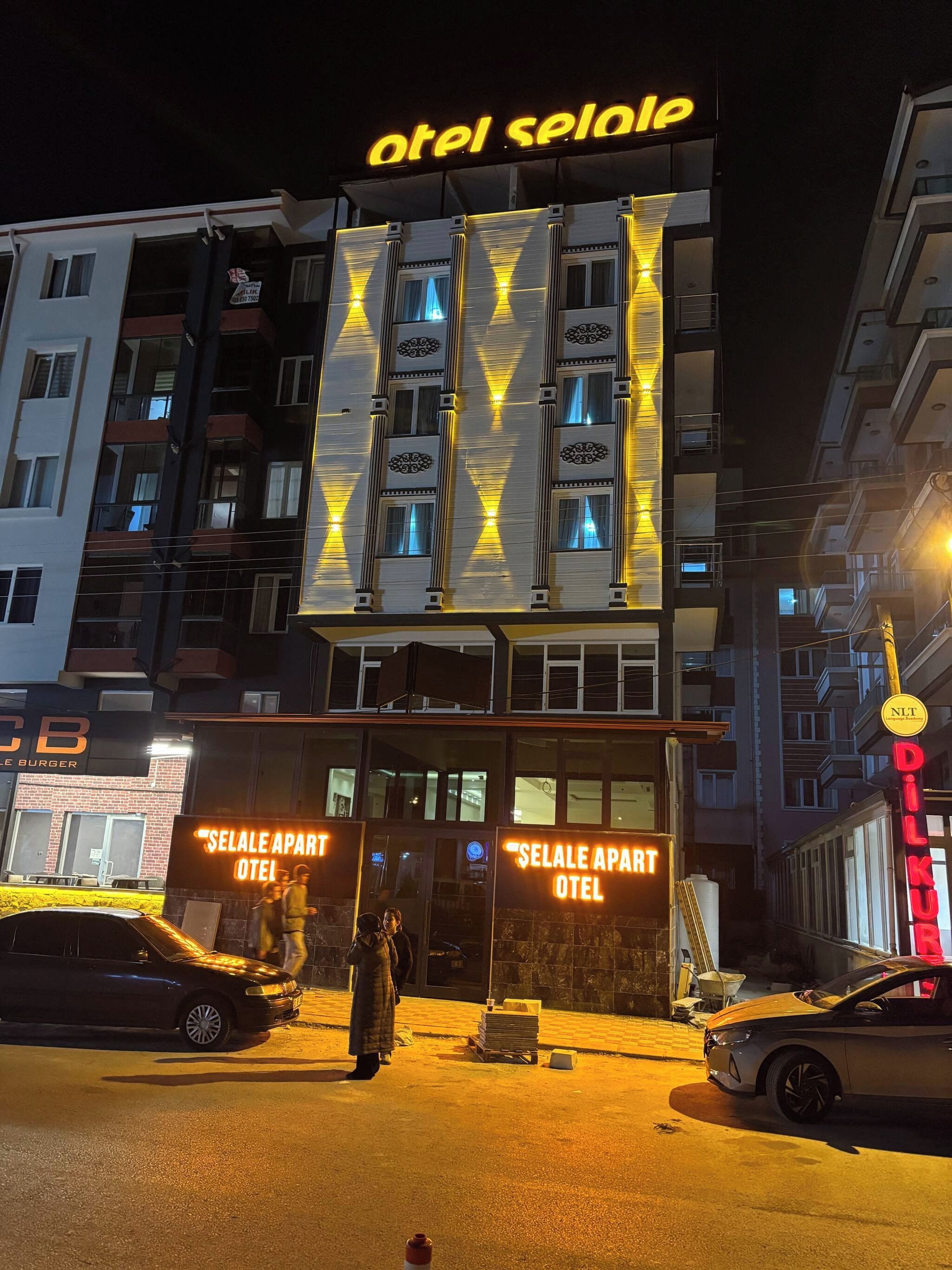 A hotel with a prominent illuminated sign, a ground-level entrance, and a visible parking area.