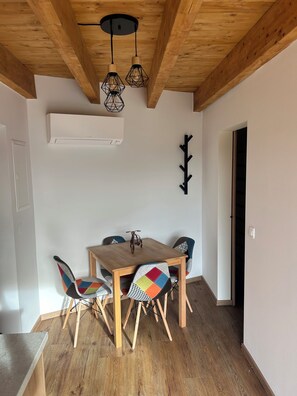 Et spiseområde med et træbord og stole, en hængende lampe og en vægmonteret aircondition.