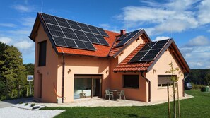 Et hus med solpaneler på taget, en garage og en terrasse med havemøbler.