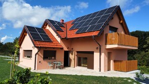 Ein Haus mit Solaranlage auf dem Dach, einem Balkon und einer Terrasse mit Gartenmöbeln.