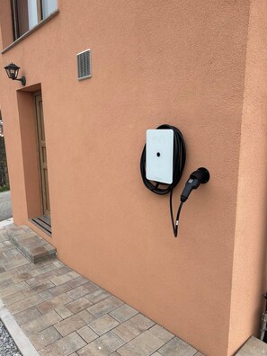 A wall-mounted electric vehicle charging station with a cable and plug. - Cozy 2-bedroom house in charming Gradišča with AC and Sauna (Cirkulane)