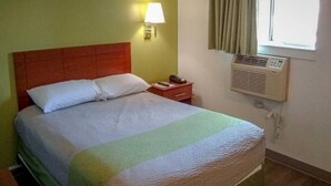 Ein Hotelzimmer mit Bett, Nachttischlampe, Beistelltisch und Klimaanlage.