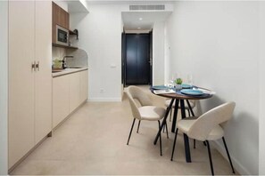 A compact kitchen with modern appliances, a dining area with a round table and chairs, and a dark door in the background. - "Cobalto" Designer Apartment (Estepona)
