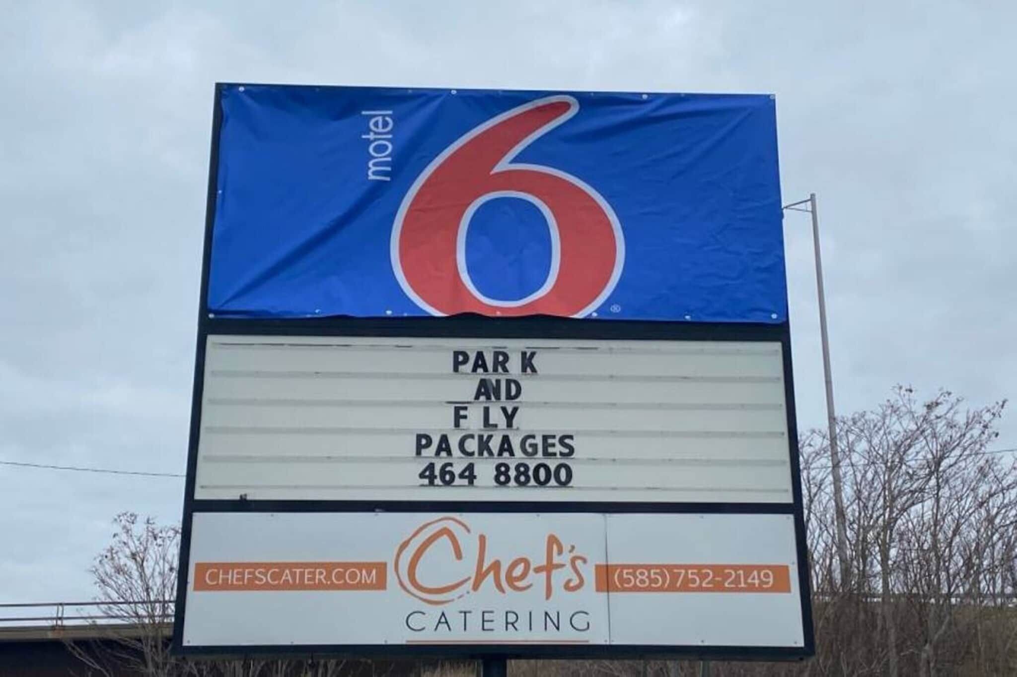 Letrero de motel con un número grande '6' y menciones de paquetes estacionamiento y vuelo, servicio de catering y una página web.