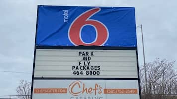 Letrero de motel con un número grande '6' y menciones de paquetes estacionamiento y vuelo, servicio de catering y una página web.