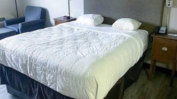 A hotel room with a large bed, a bedside table with a lamp, a chair, and a nightstand with a phone.
