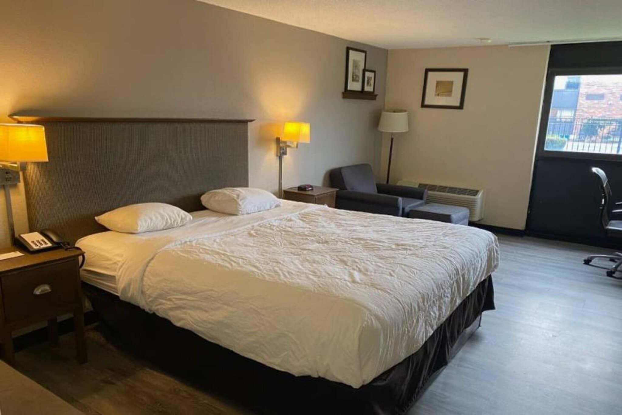 Een hotelkamer met een groot bed, bedlampen, een stoel en een bureau met een telefoon.