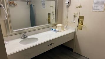 Een hotelbadkamer met een grote spiegel, een wastafel, een handdoekrek, een haardroger en een vel papier aan de muur.