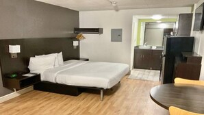 A hotel room with a bed, bedside table, lamp, and a small desk with a chair. - 1 King Bed|Smoking| Kitchen (Columbus GA)