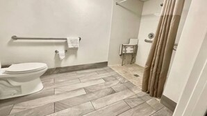 A bathroom with a toilet, a handrail, a shower curtain, and a tiled floor. - 1 King Bed Non-Smoking Kitchen (Columbus GA)