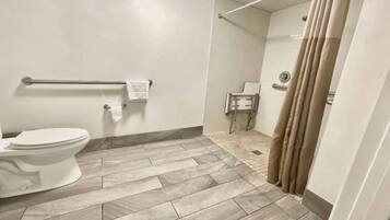 A bathroom with a toilet, a handrail, a shower curtain, and a tiled floor.