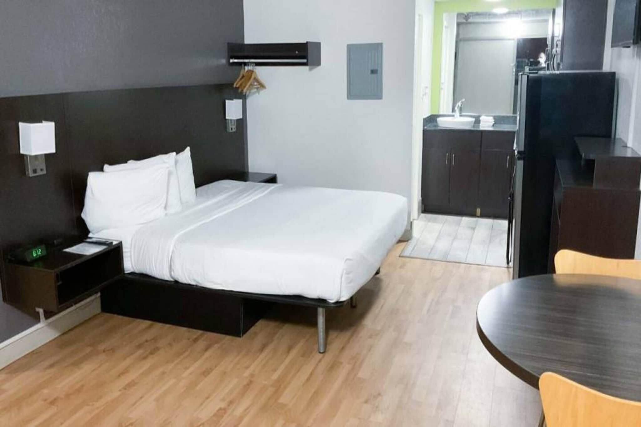 A hotel room with a bed, bedside table, lamp, and a small desk with a chair.