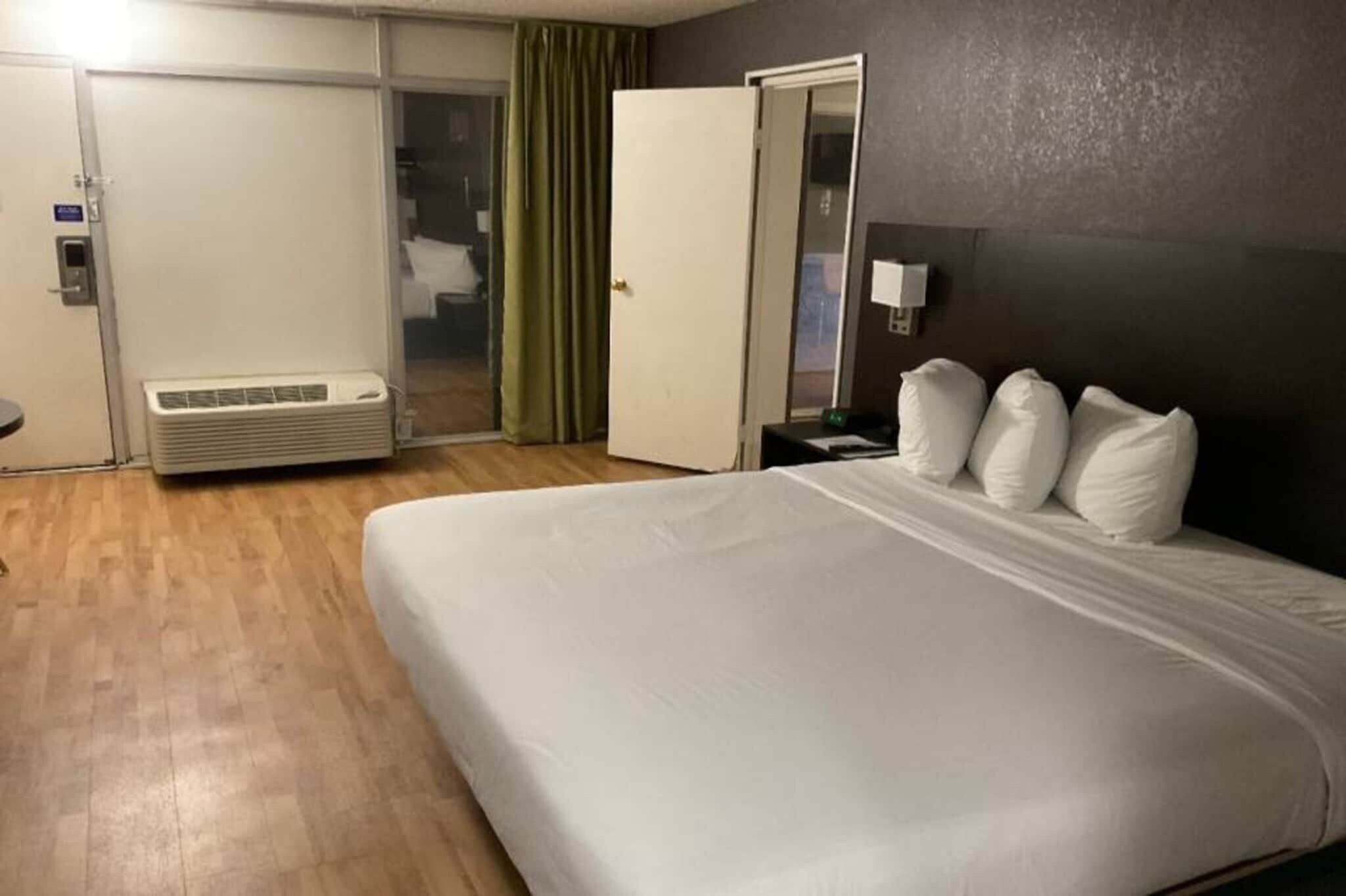 Ein Hotelzimmer mit einem großen Bett, einem Nachttisch, einer Lampe und einer Schiebetür, die auf einen Balkon führt.