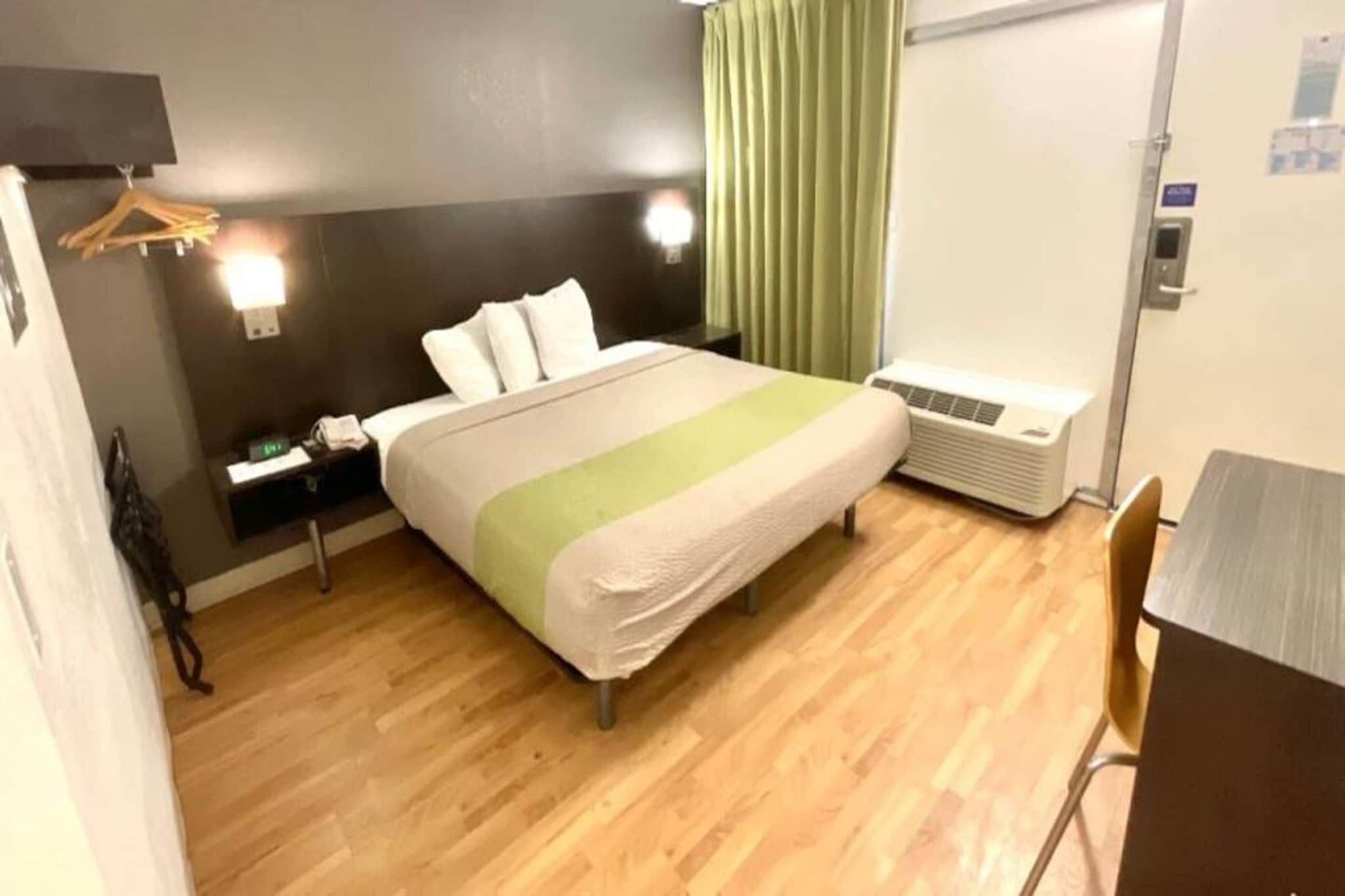 Une chambre d’hôtel comprenant un lit, une table de chevet, une lampe, un appareil de climatisation et une chaise.
