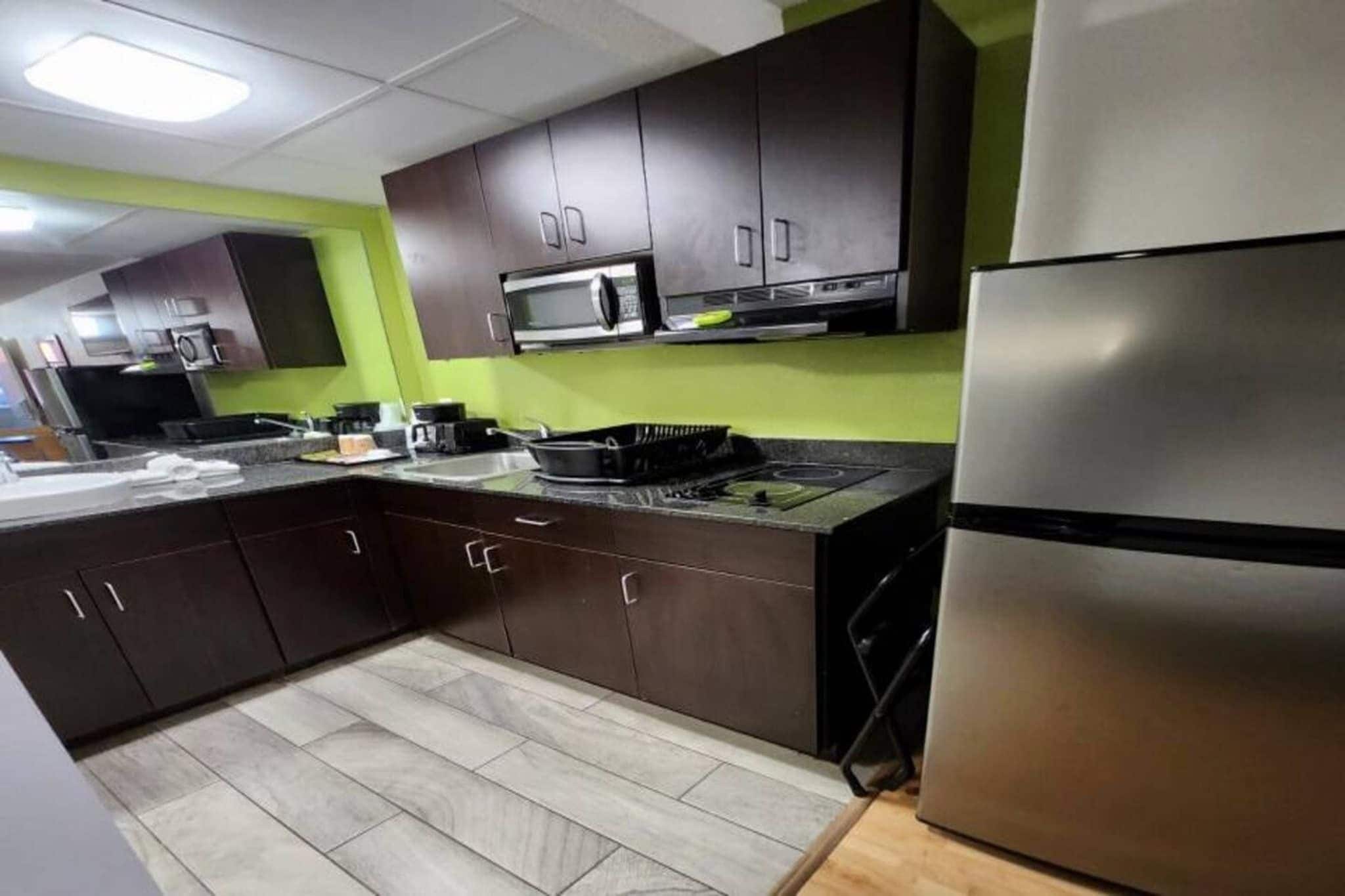 A kitchen with dark cabinets, a stainless steel refrigerator, and a microwave.