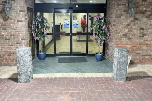 Entrada de hotel con fachada de ladrillo, puertas dobles y dos macetas a cada lado.