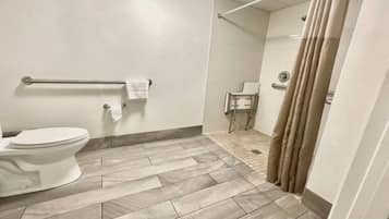 A bathroom with a toilet, a handrail, a towel rack, and a shower curtain.