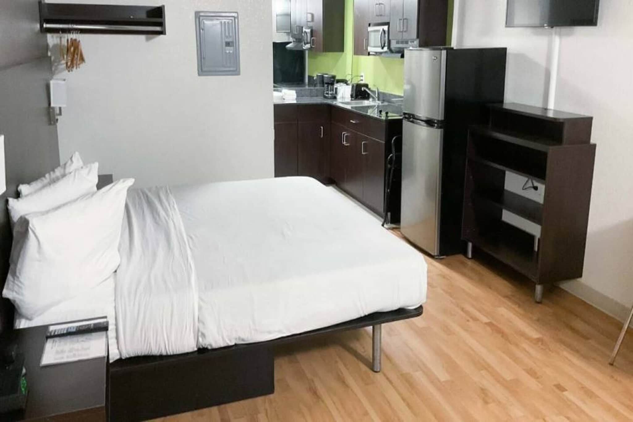 Ein kleines Hotelzimmer mit Bett, einer kleinen Küchenzeile und einem Fernseher.