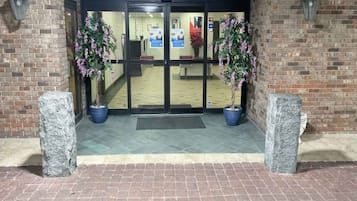 A hotel entrance with a brick facade, double doors, and two potted plants.