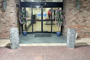 A hotel entrance with a brick facade, double doors, and two potted plants. - 1 King Bed | Mobil Access Tub Nsmk Kitchen (Columbus GA)