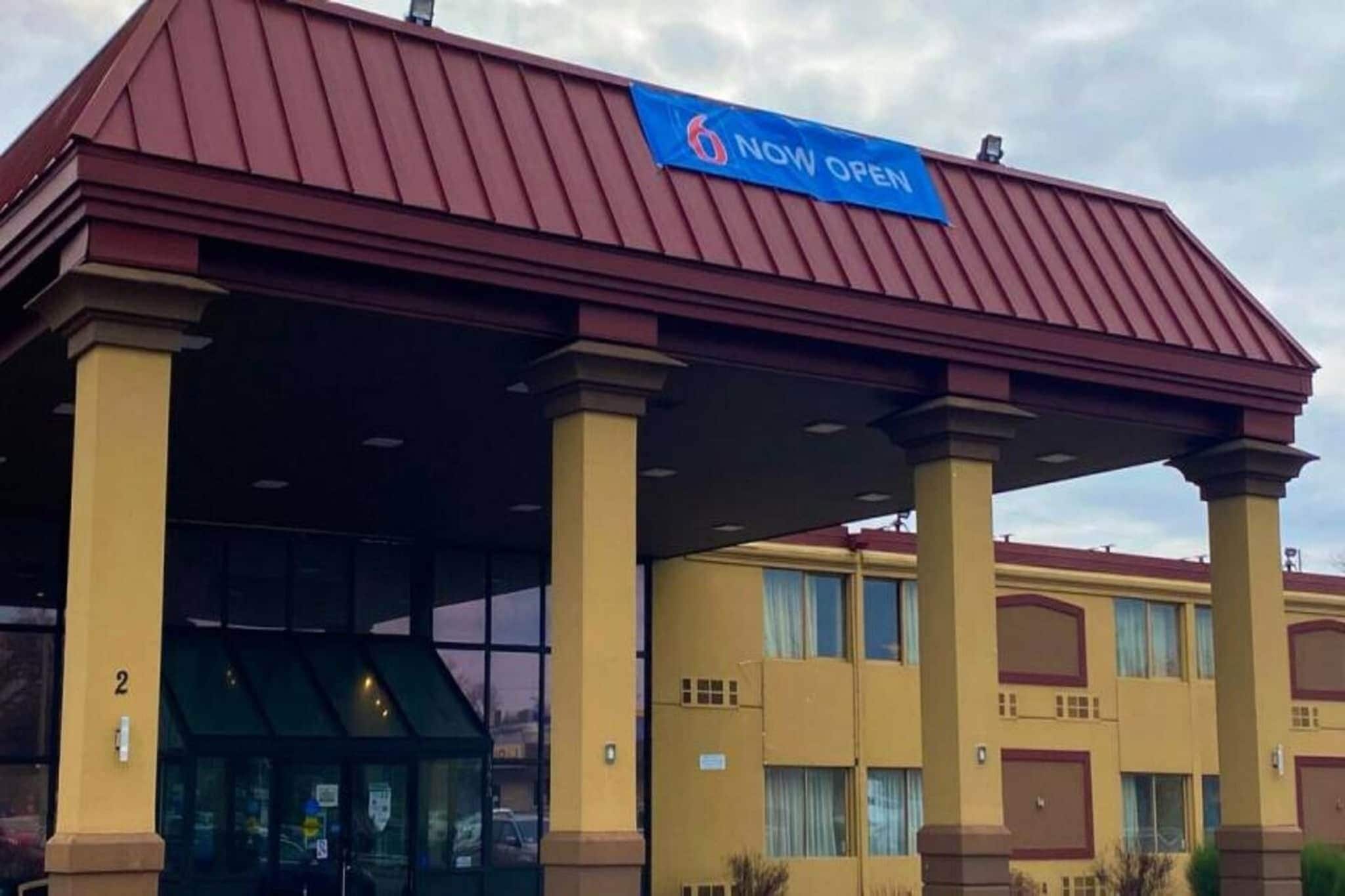 Een hotel met een 'NU OPEN' bord, een overdekte ingang en het nummer '2' op het gebouw.