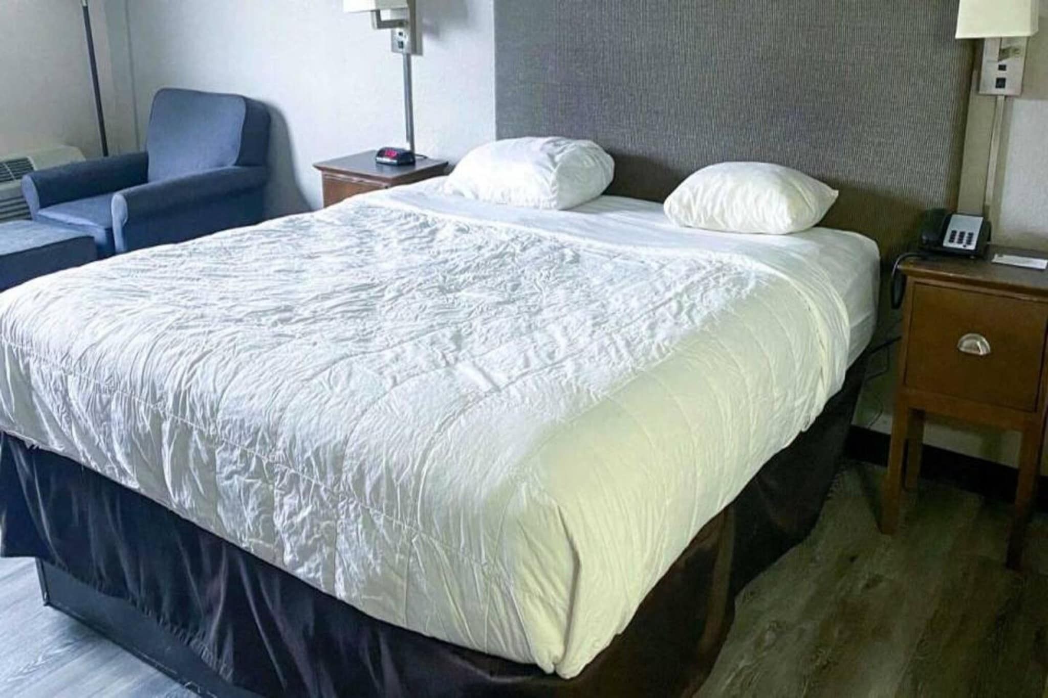 A hotel room with a large bed, a bedside table with a lamp, a chair, and a nightstand with a phone.