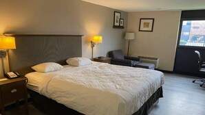 Quarto de hotel com uma cama grande, luminárias de cabeceira, uma cadeira e uma escrivaninha com telefone.