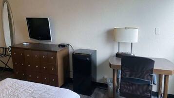 A hotel room with a bed, a dresser, a desk with a lamp, a television, and a refrigerator.
