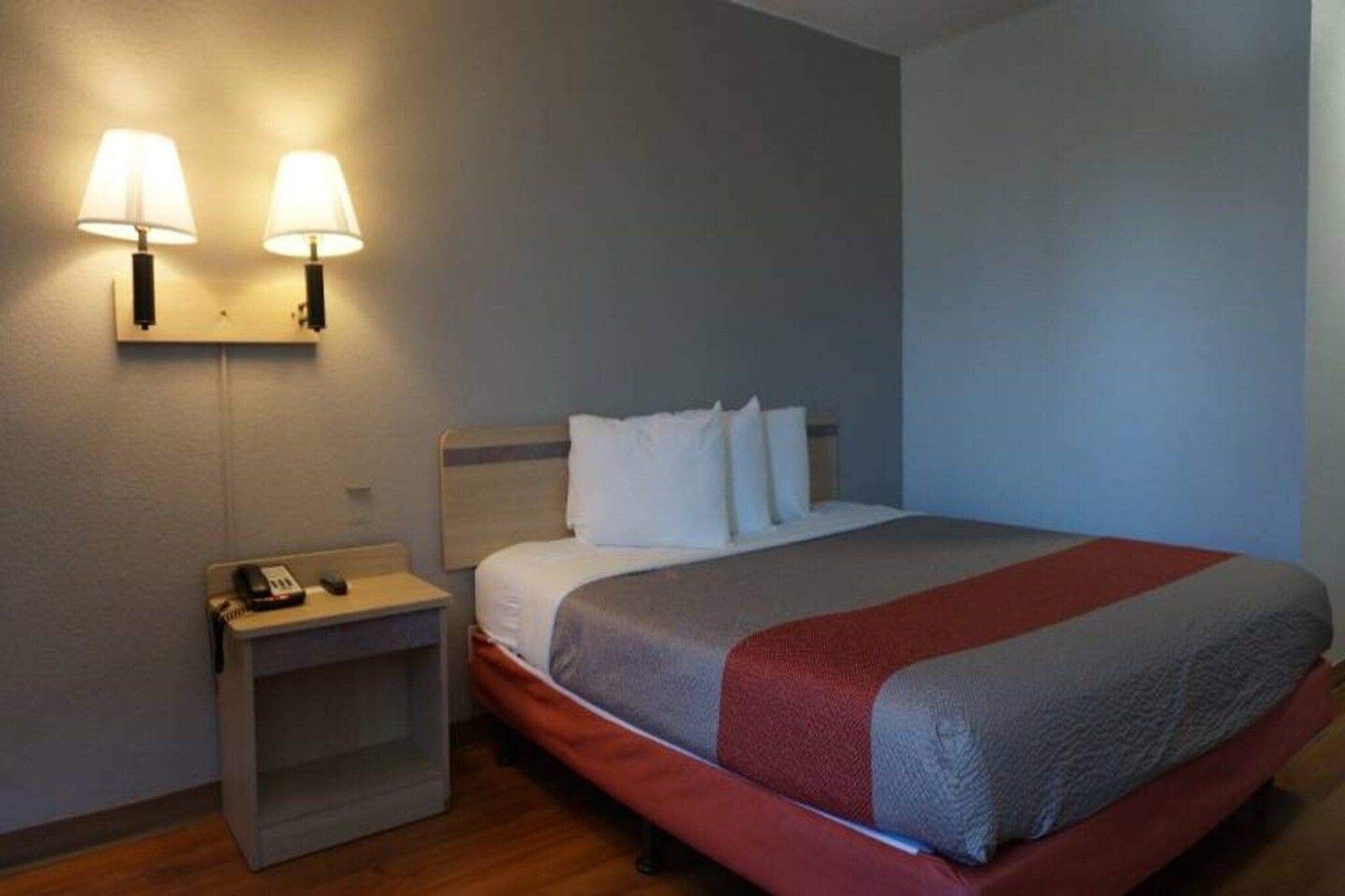 A hotel room with a bed, two bedside lamps, a nightstand with a phone, and a wall-mounted light fixture.