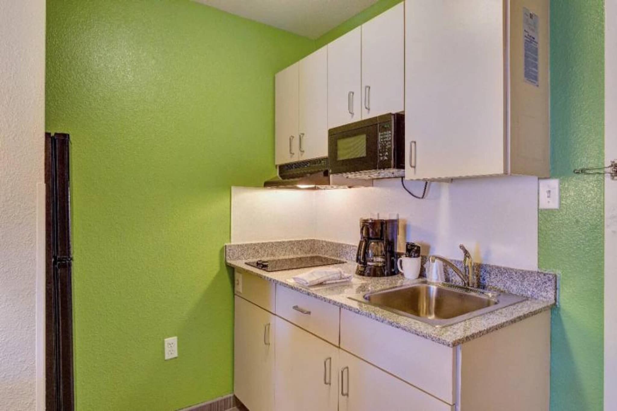 A compact kitchen with white cabinets, a stainless steel sink, and a microwave.