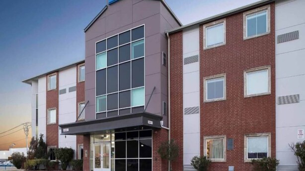 A multi-story hotel with a prominent '6' sign on the roof, large windows, and a brick facade. - 2 Full Beds | Non-Smoking, Micfridge (Norman)