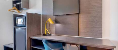 A modern room with a desk, chair, TV, and a small kitchenette.
