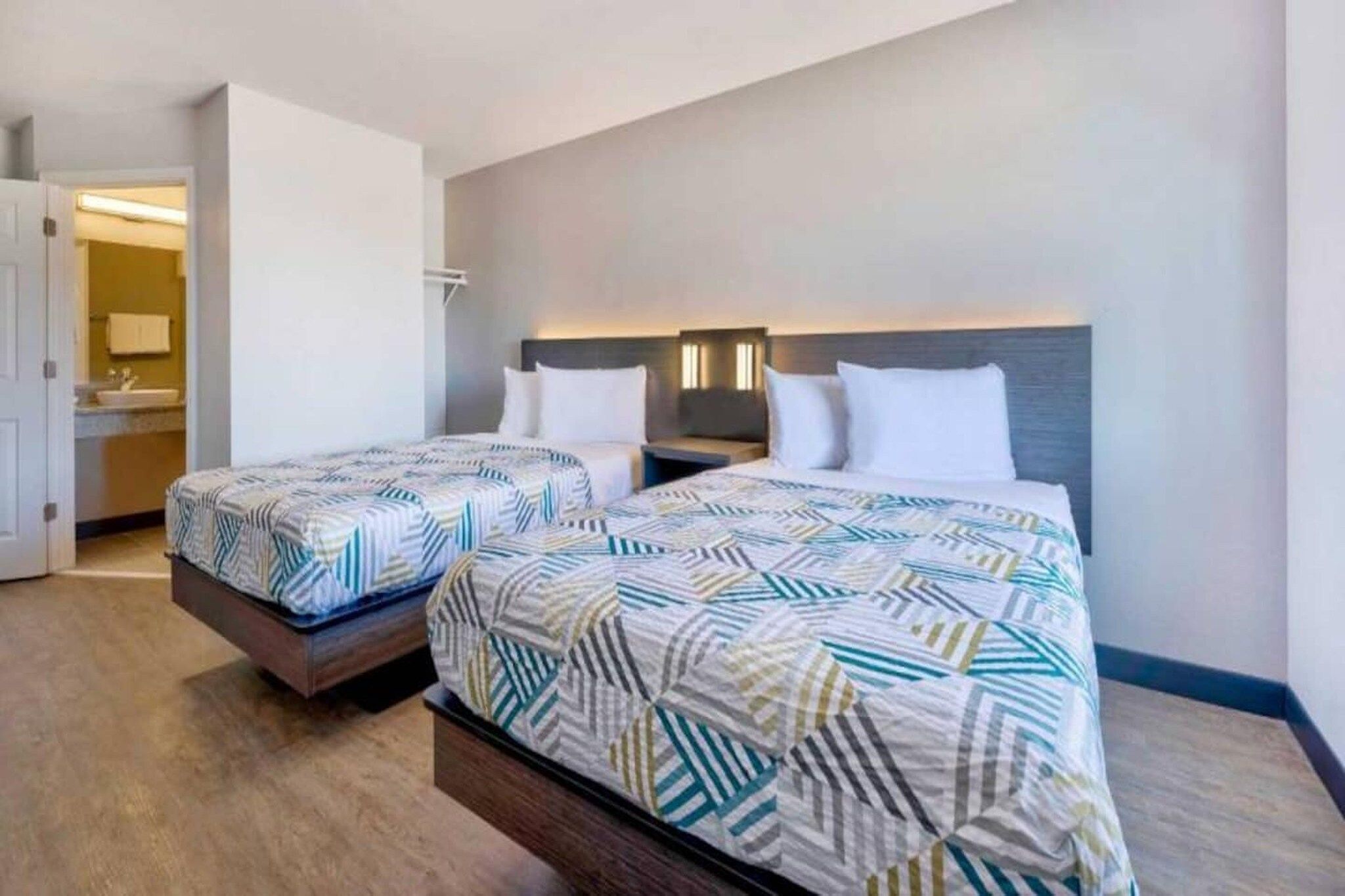 A hotel room with two beds, a bathroom, and a hallway.