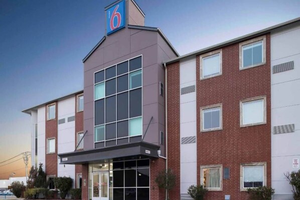A multi-story hotel with a prominent '6' sign, large windows, and a brick facade. - 1 King Bed | Non-Smoking, Micfridge (Norman)