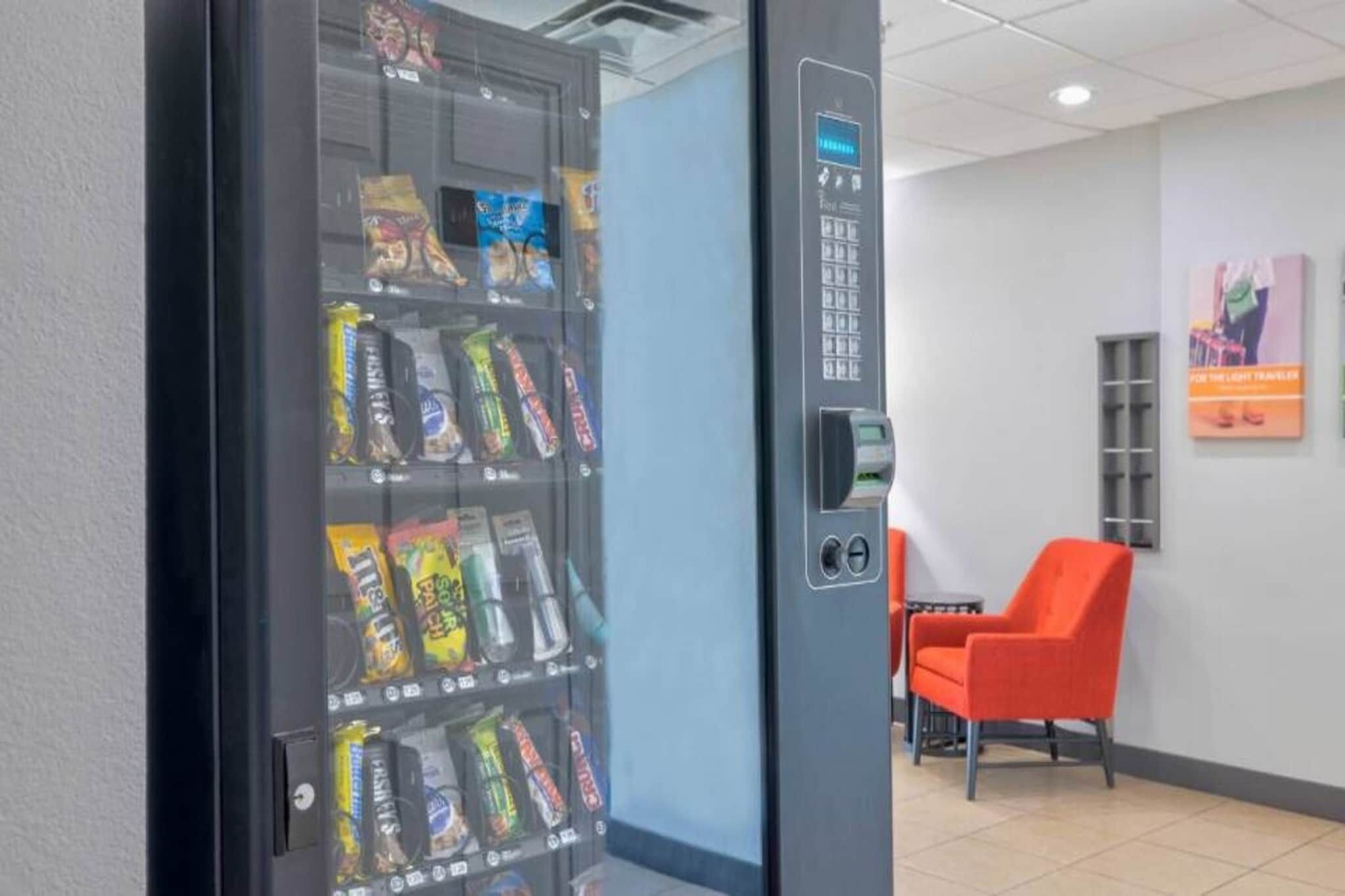 Un distributeur automatique de collations, un terminal de paiement et un espace détente avec des chaises orange.
