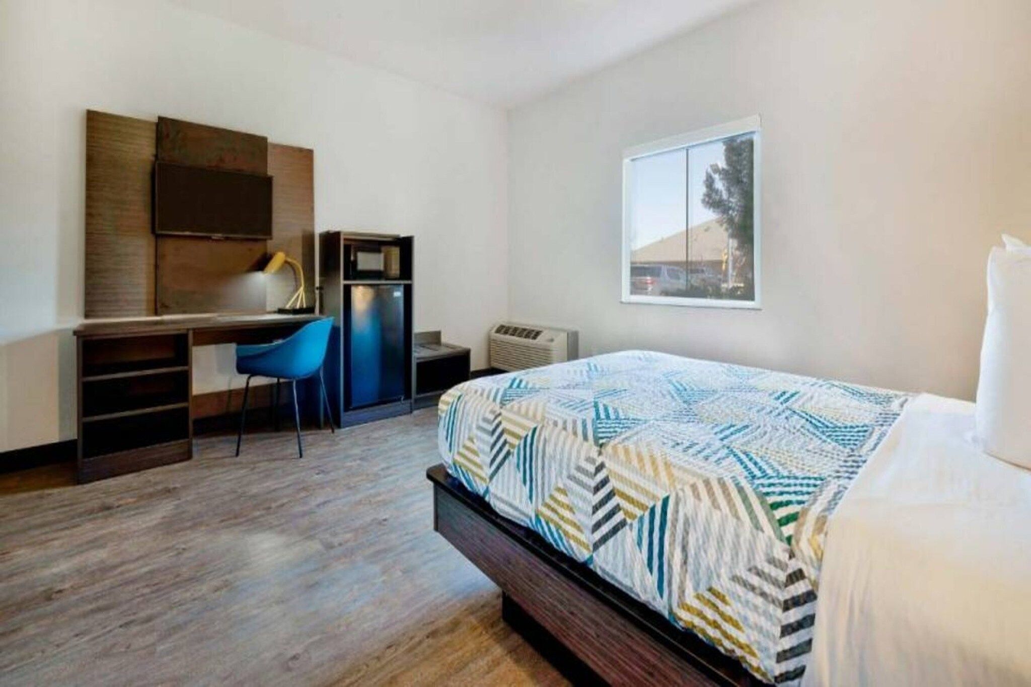 Une chambre à coucher avec un lit, un bureau, une chaise, une armoire et une fenêtre.