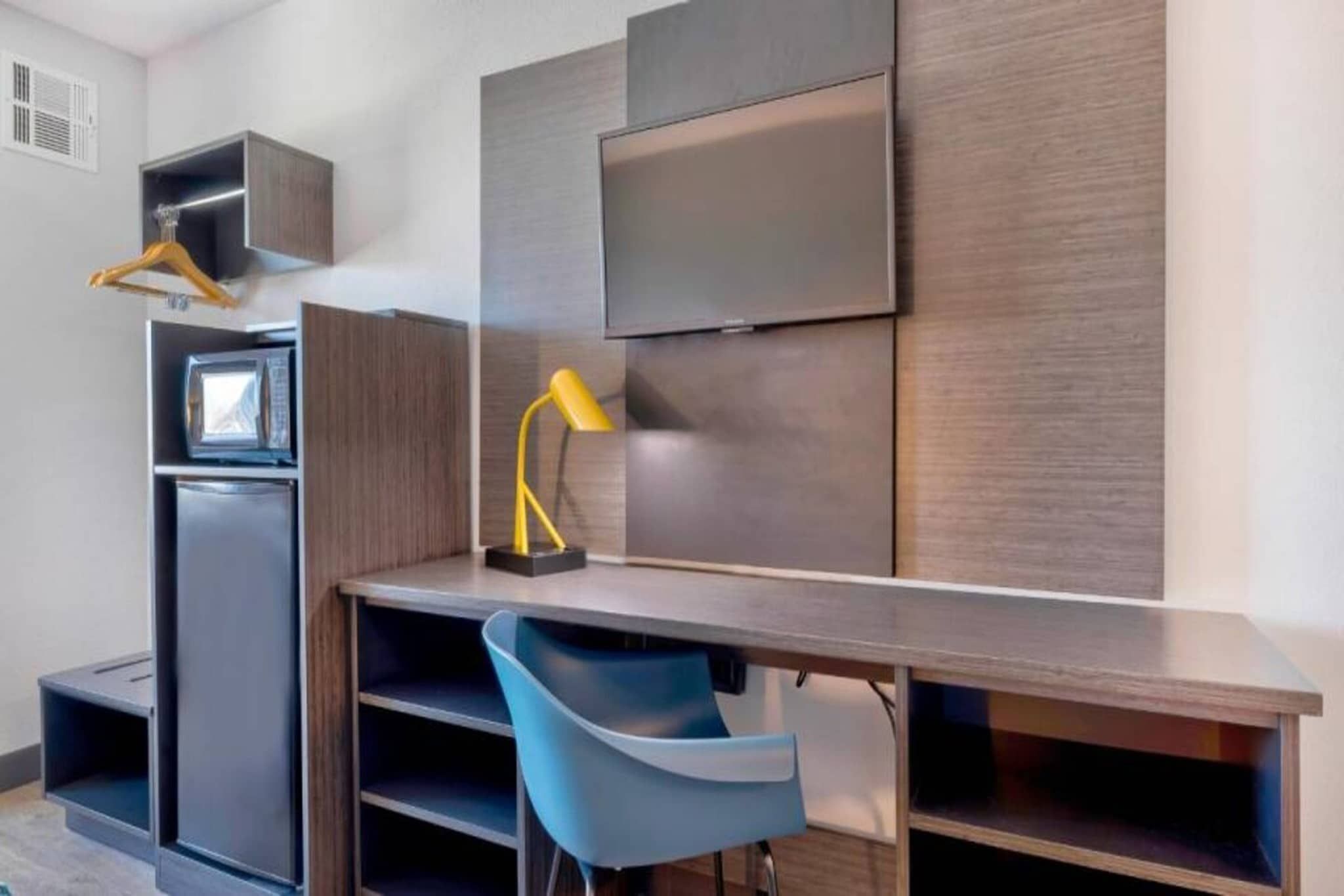 Une chambre moderne équipée d’un bureau, d’une chaise, d’une télévision et d’une petite kitchenette.